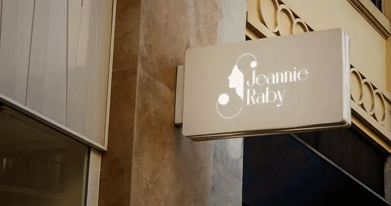 A white wall-mounted sign for Jeannie Raby featuring a woman's profile silhouette logo.