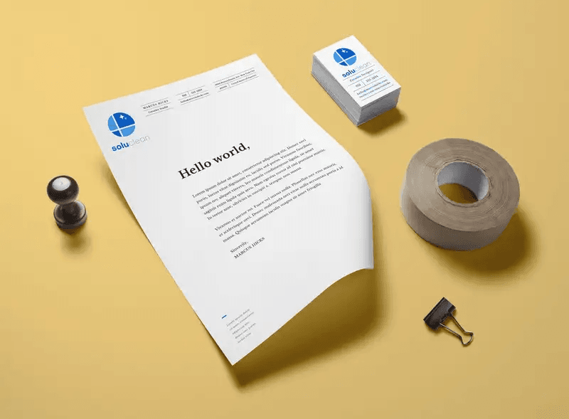 Branded letterhead, business cards, a stamp, tape, and a binder clip on a yellow surface.