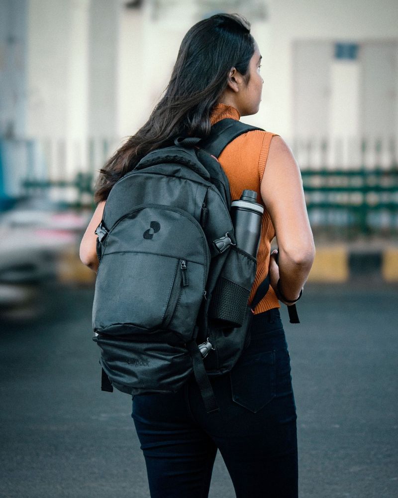 A woman from behind wearing an orange sleeveless top and a black backpack.