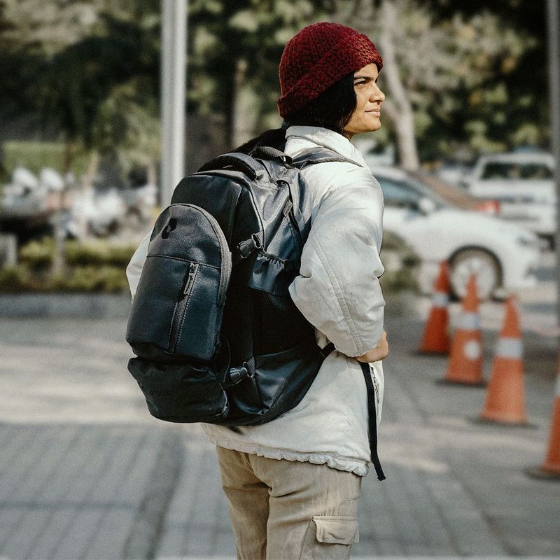 Person in a red beanie and white jacket wearing a large black backpack outdoors.