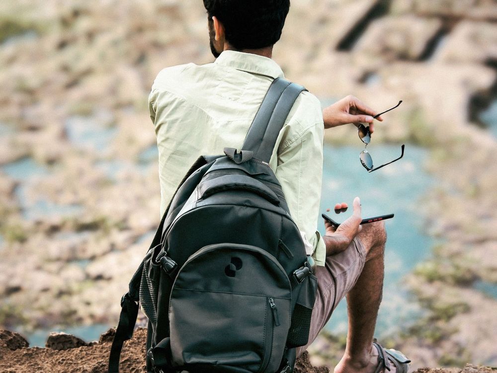 A man with a backpack sits on a rocky cliff overlooking a tide pool.