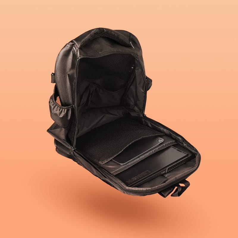 An open black backpack floating against a peach background, showing a laptop and tablet inside.