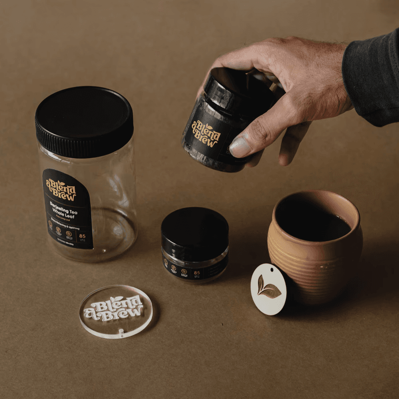 Hand holding a black tea jar next to various Blend & Brew tea containers.