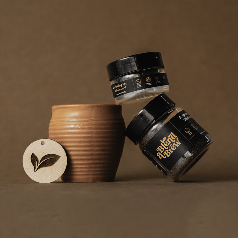 Balanced jars of Blend and Brew Darjeeling tea stacked beside a clay tea cup.