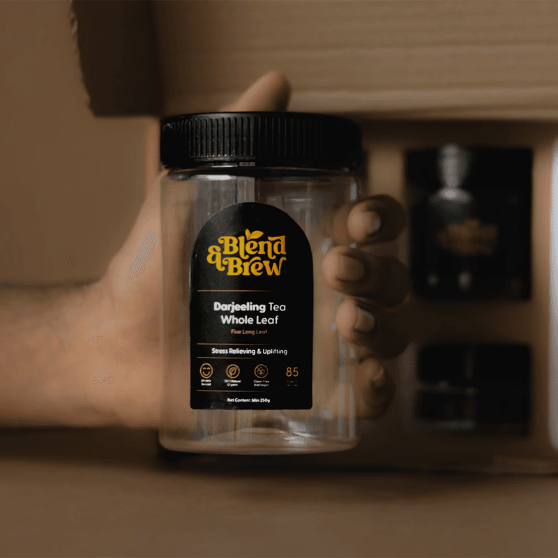 Hand holding a clear jar of Blend & Brew Darjeeling whole leaf tea.