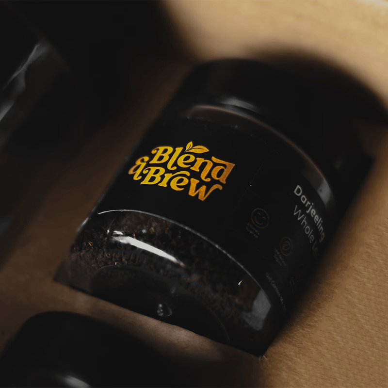 Close-up of a Darjeeling tea jar with a gold Blend & Brew logo inside a box.