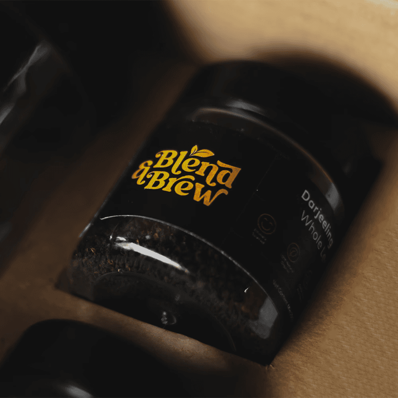 Close-up of a Darjeeling tea jar with a gold Blend & Brew logo inside a box.