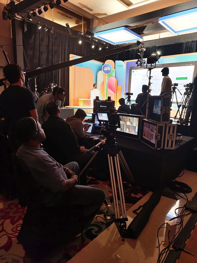 Video production crew operating cameras and monitors in front of a colorful stage backdrop.