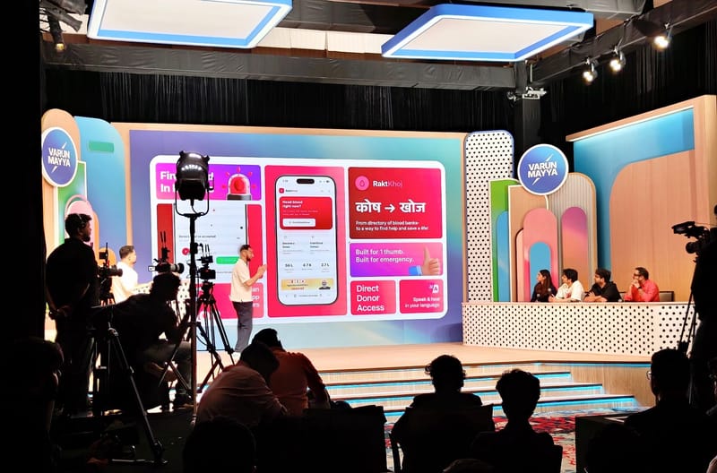 A man presents a blood donation app on a large screen to judges and cameras.
