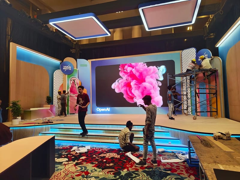 Workers assembling a stage with a large screen showing pink smoke and OpenAI logo.