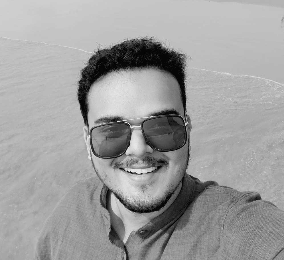 Black and white selfie of a smiling man with sunglasses on a beach.
